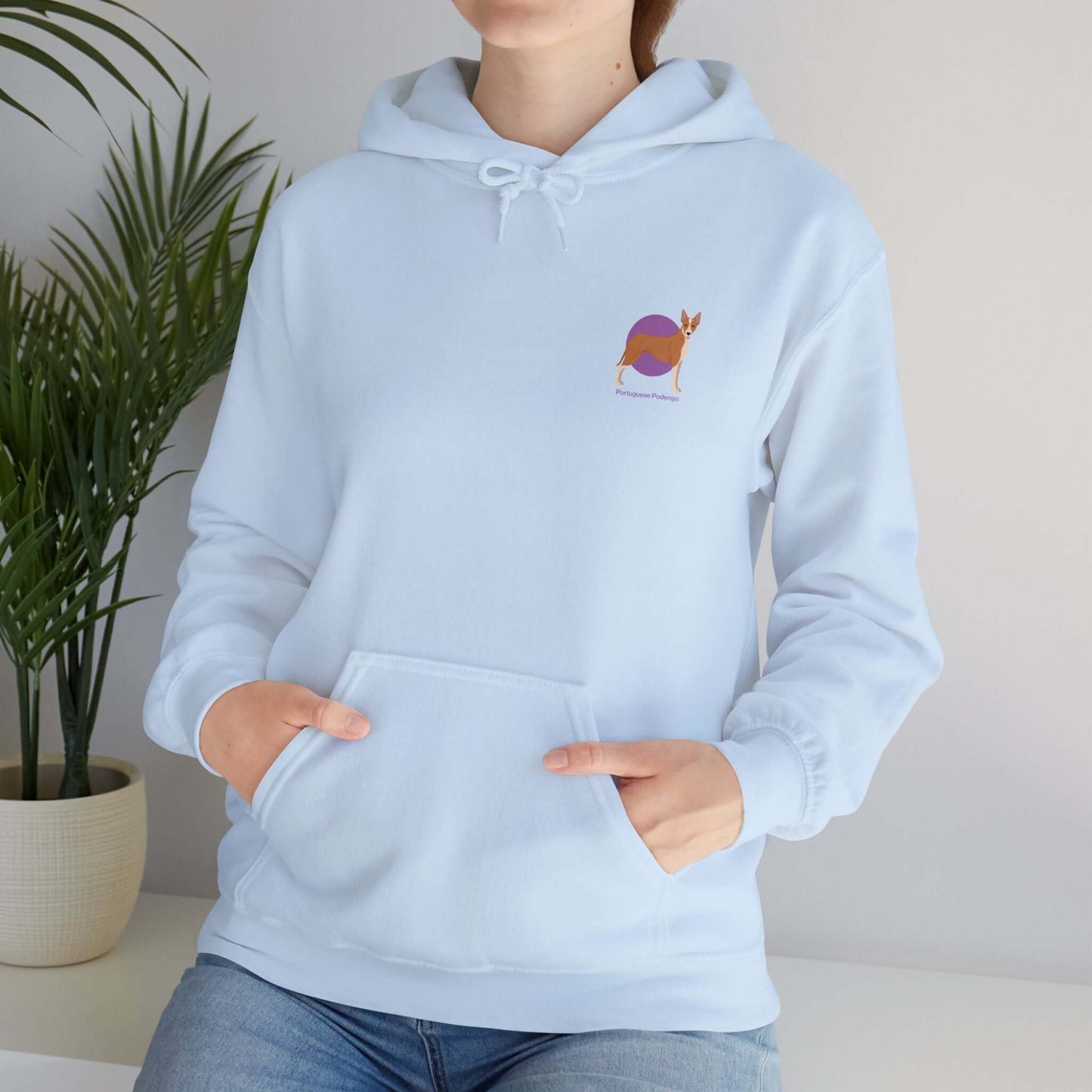 Woman wearing a light blue Portuguese Podengo hoodie with dog logo, standing indoors next to a green plant.