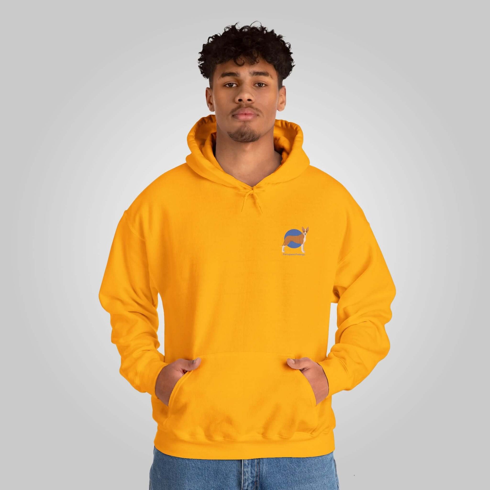 Young man wearing a yellow Portuguese Podengo graphic hoodie, hands in pockets, looking at camera.