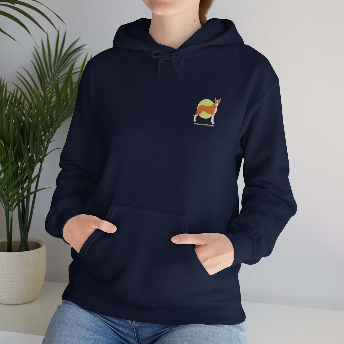 Woman wearing a navy blue Portuguese Podengo hooded sweatshirt, with dog design on chest, standing indoors near a plant.